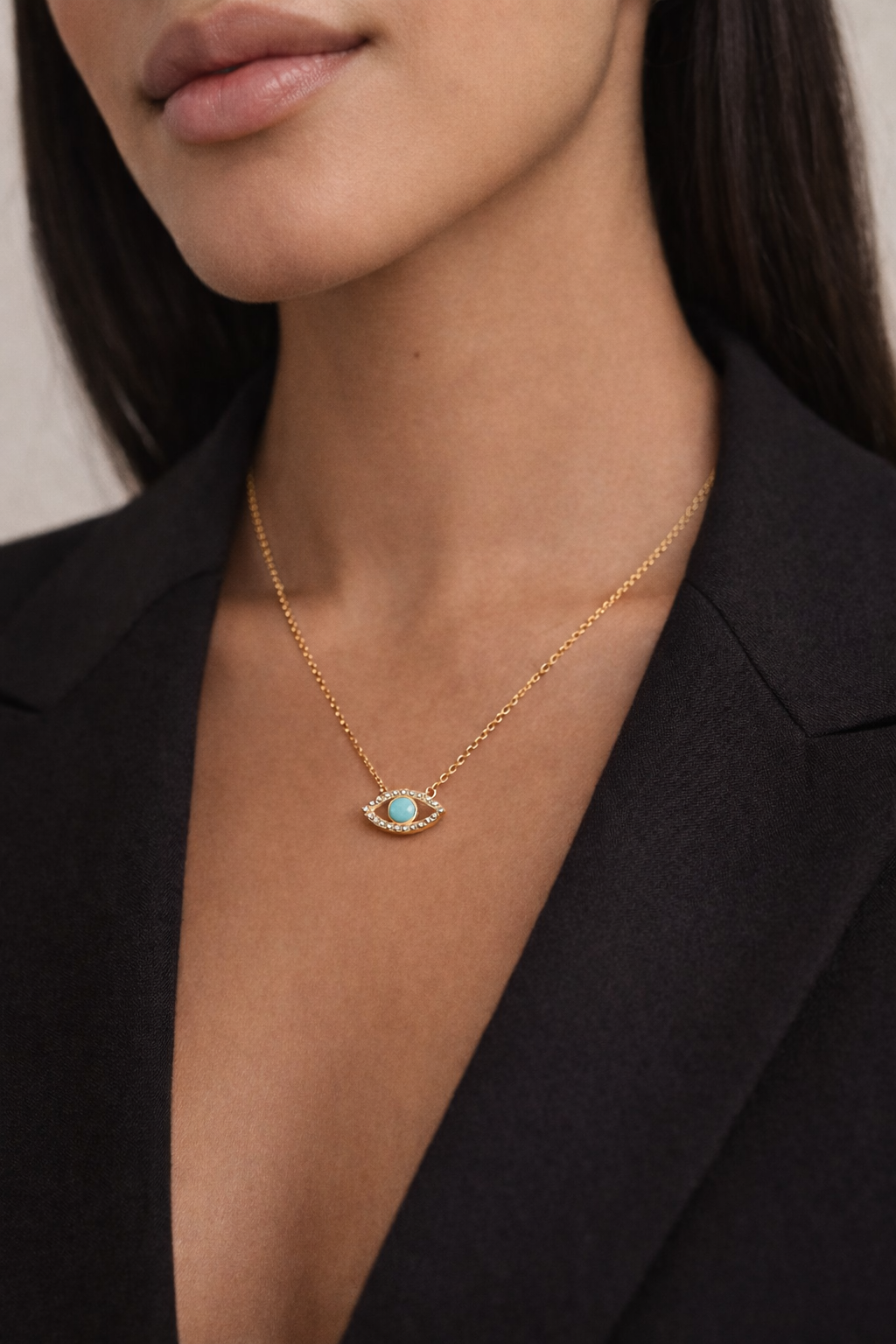 Gold necklace with a turquoise eye pendant worn by a person in a black blazer.